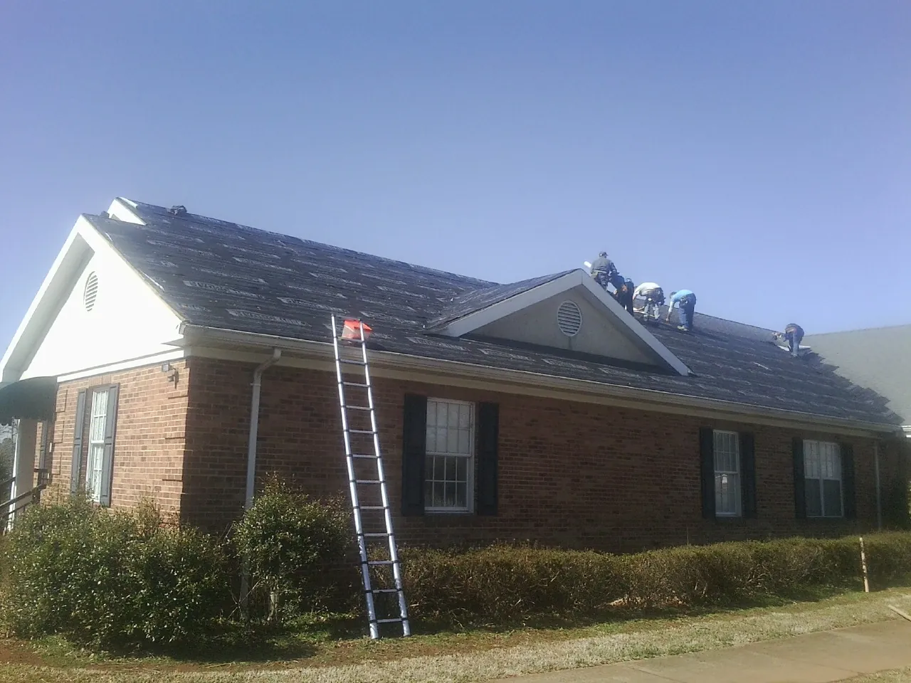 Crew tearing shingles off a brick ranch roof with a ladder set — Metal Roof Repair work by our crew in Ovid