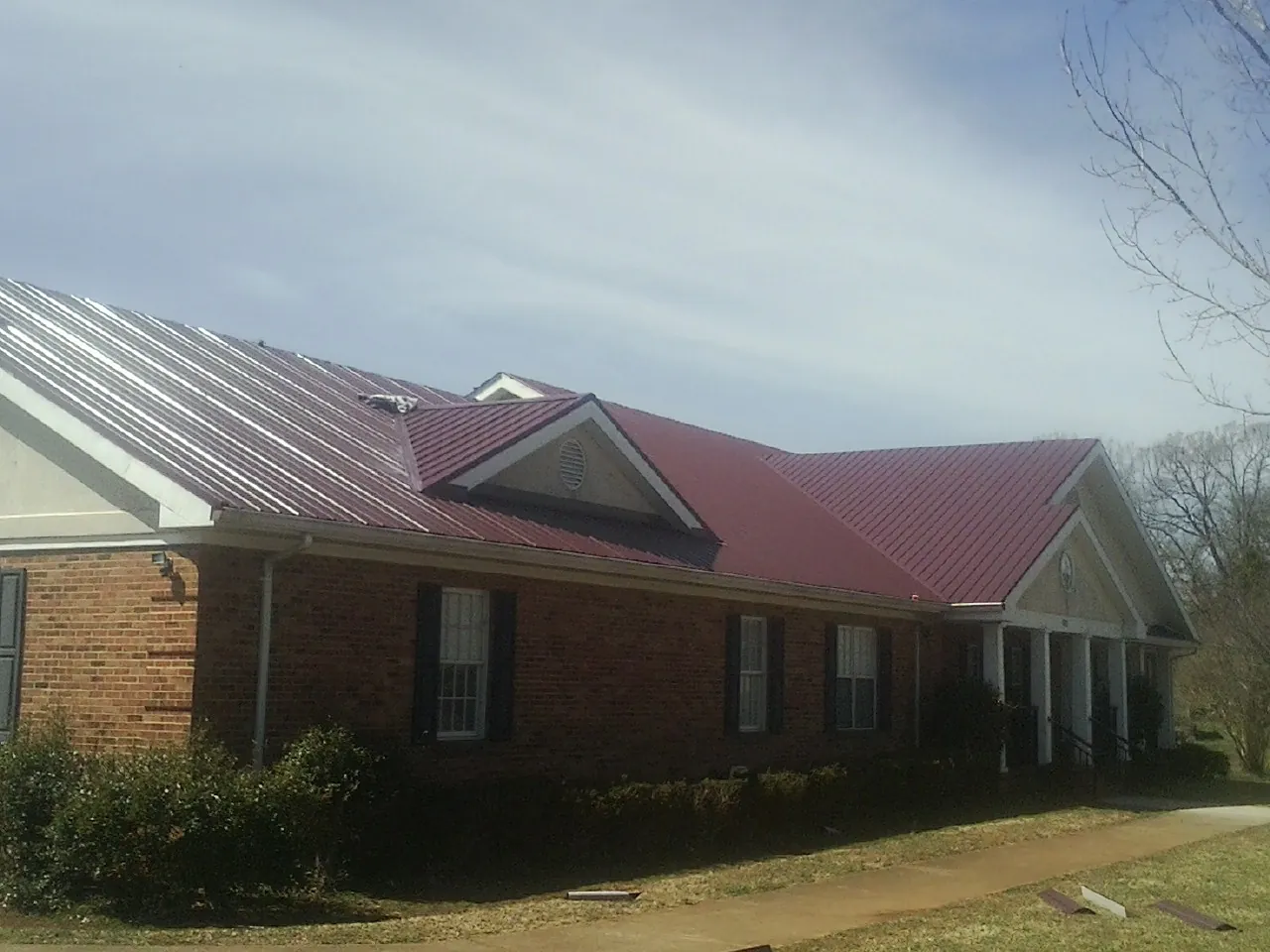 Red metal roof with gabled entries on a long brick building, from a Hail Damage Roof Repair job in Ovid