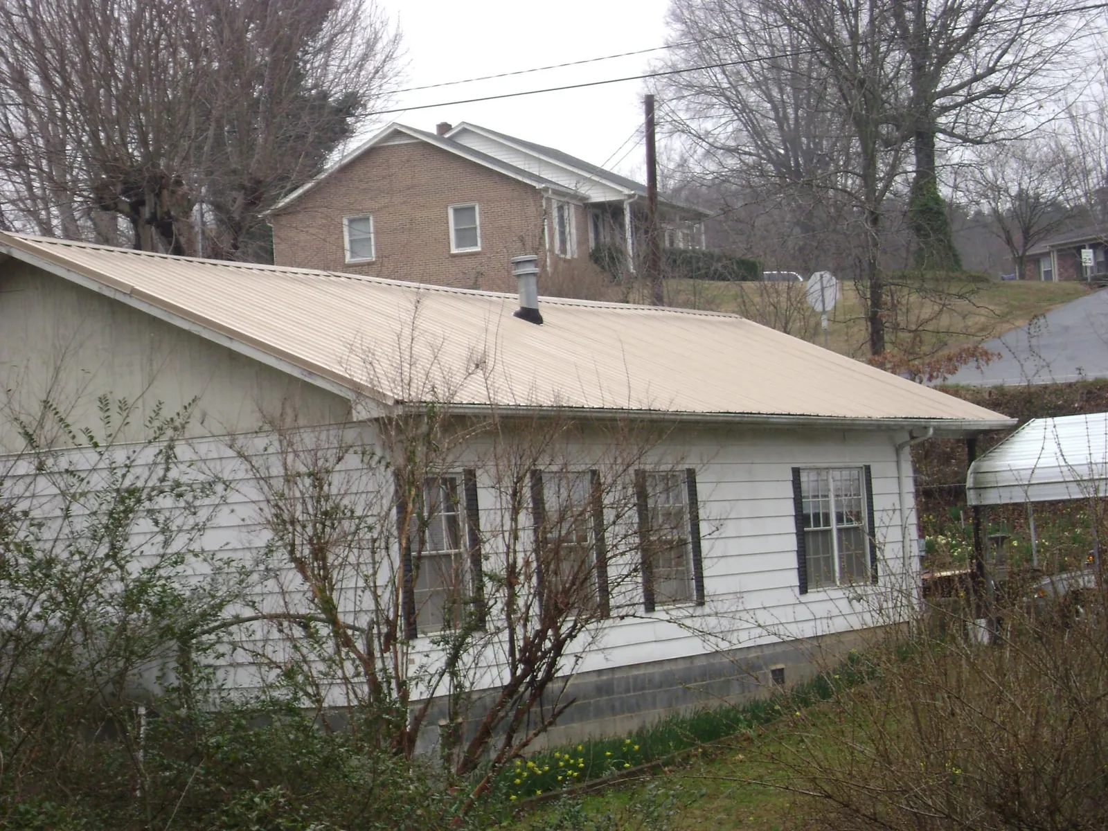 Tan metal roof on a white sided house set into a hillside — Commercial Roofing by Roofing Brothers in Ovid